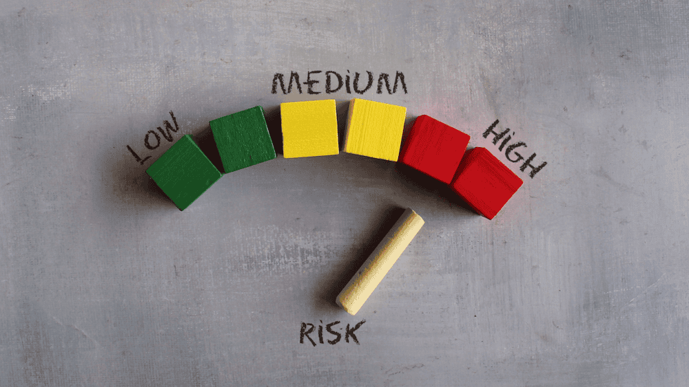 Image of risk concept with a meter made up of green, yellow and red blocks labeled low, medium and high. A wooden stick point labeled "risk" points to the red blocks labeled "high"